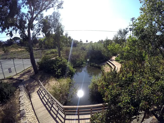 The creek and wooden boardwalk at Cottonwood Creek Park, with the tennis courts behind